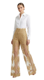 Woman wearing a white shirt and gold embroidered pants on a white background