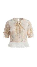 Sheer blouse with floral patterns and ruffled details on a white background