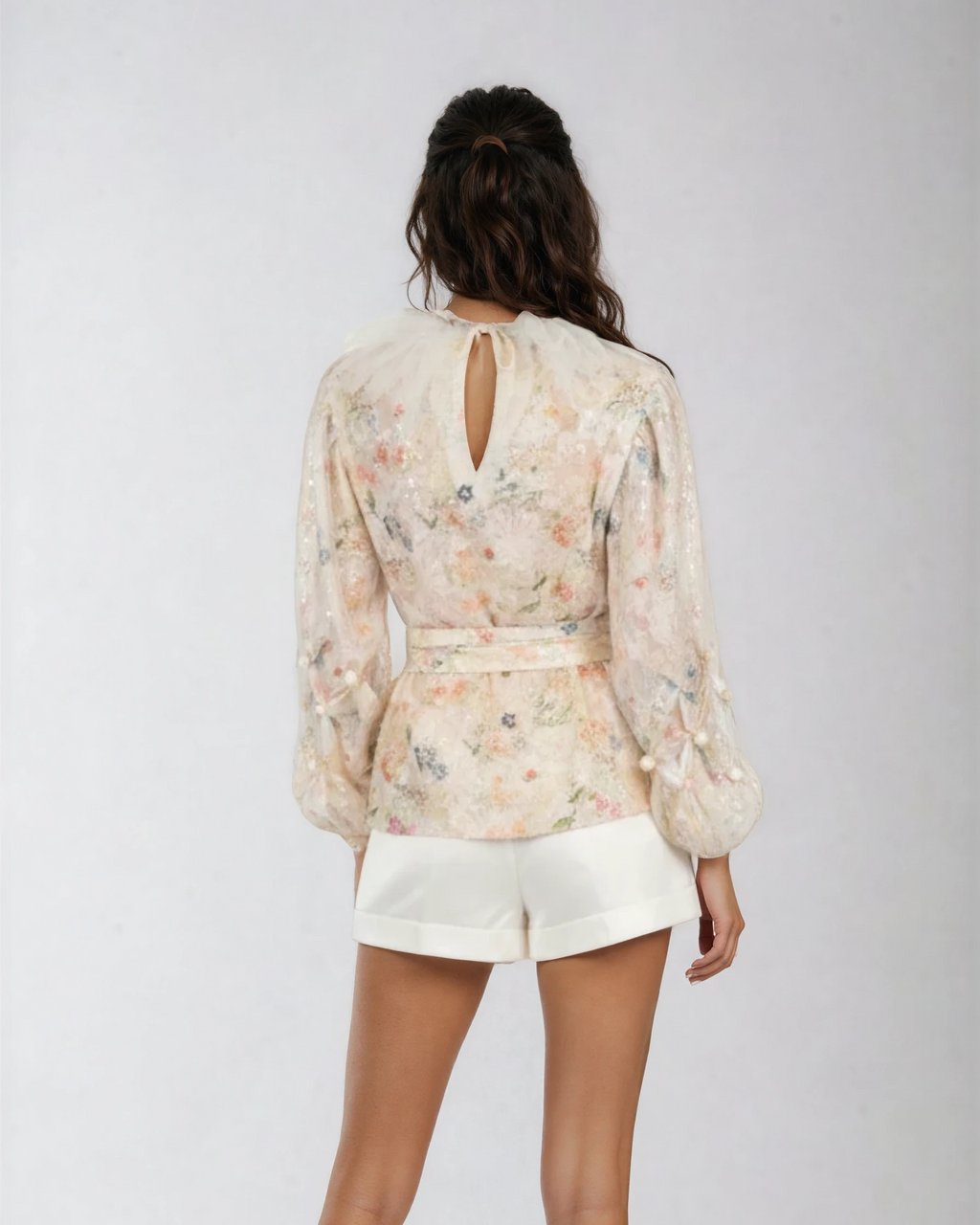 Woman wearing a floral blouse and white shorts on a plain background