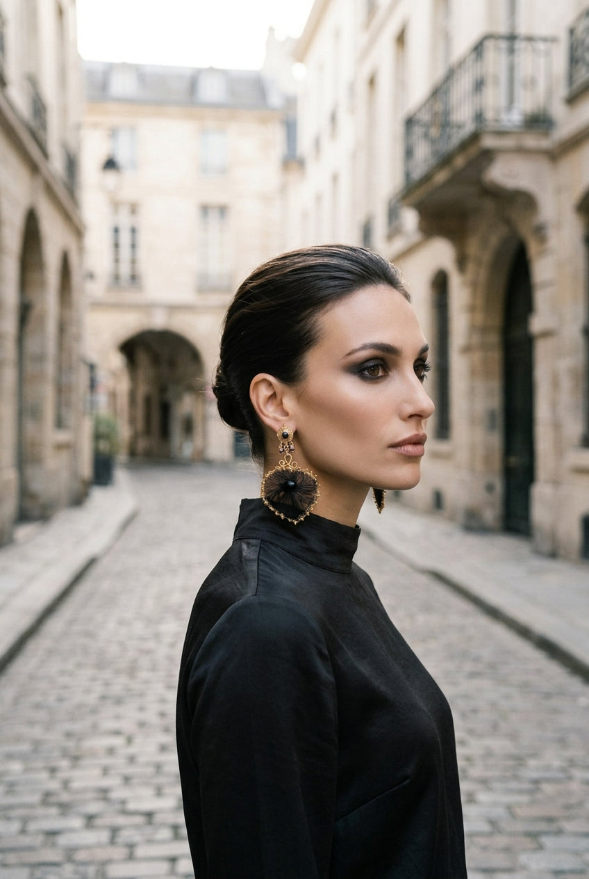 A woman in profile wearing a large ornate gold and black dangle earring, photographed against a dark draped studio background.